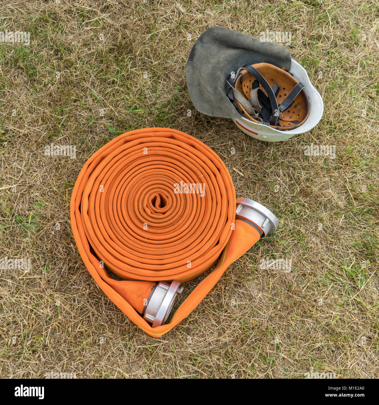 Orange fire il tubo flessibile e il casco di sicurezza si trovano sul prato Foto Stock
