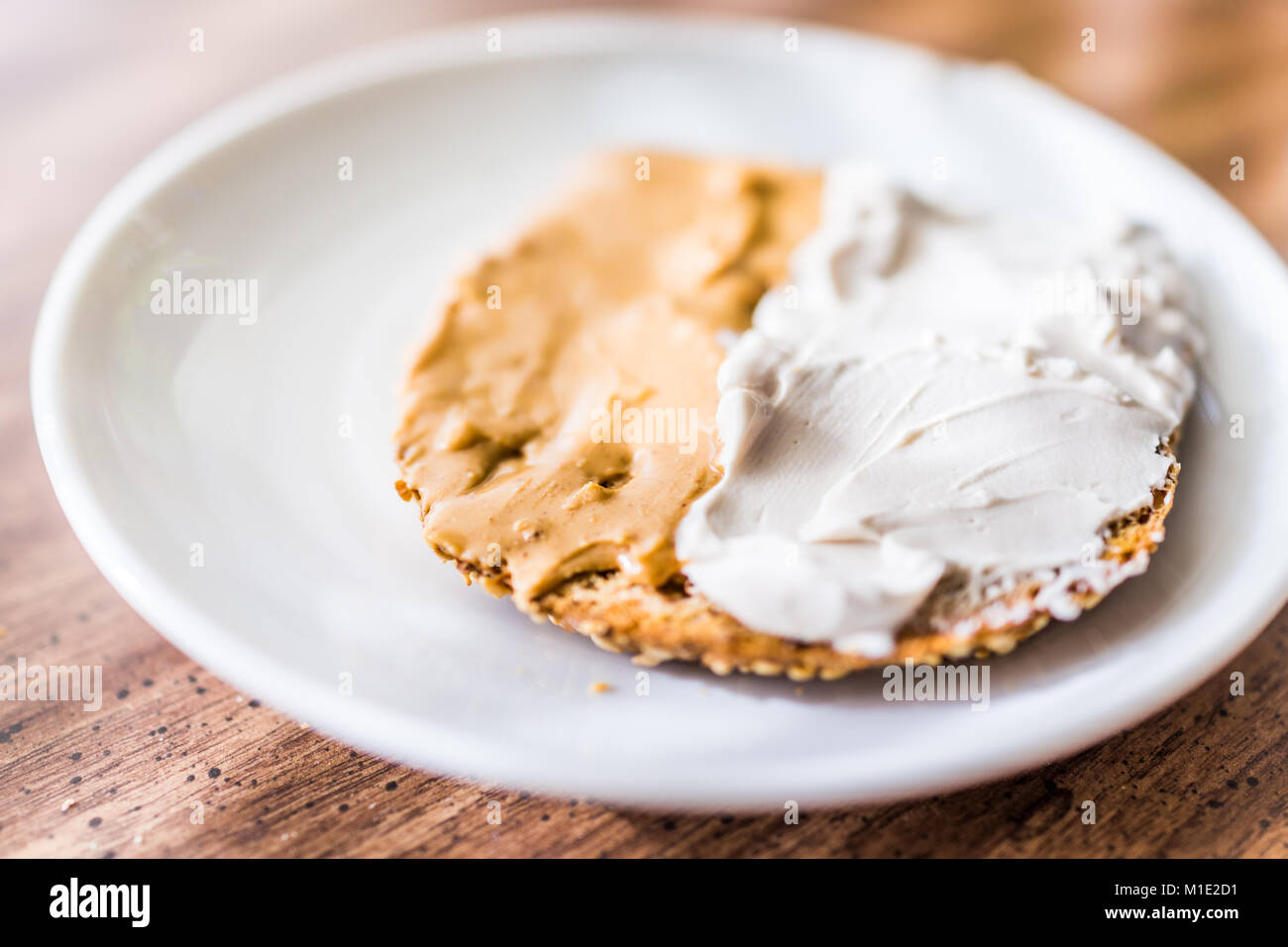 Primo piano della fetta pezzo di tutto il grano germogliato tostati Pane di grano sulla piastra con il bianco crema di formaggio sparsi sul tavolo macro, burro di arachidi Foto Stock