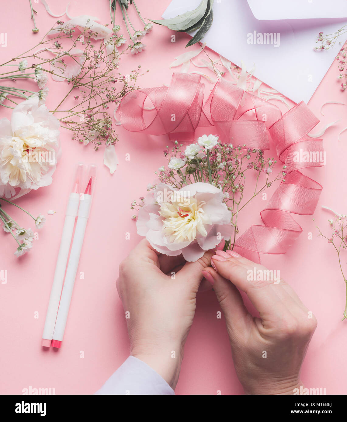 Mani femminili rendendo composizioni floreali con fiori di colore bianco e il nastro di inchiostro a colore rosa pastello sfondo, vista dall'alto Foto Stock