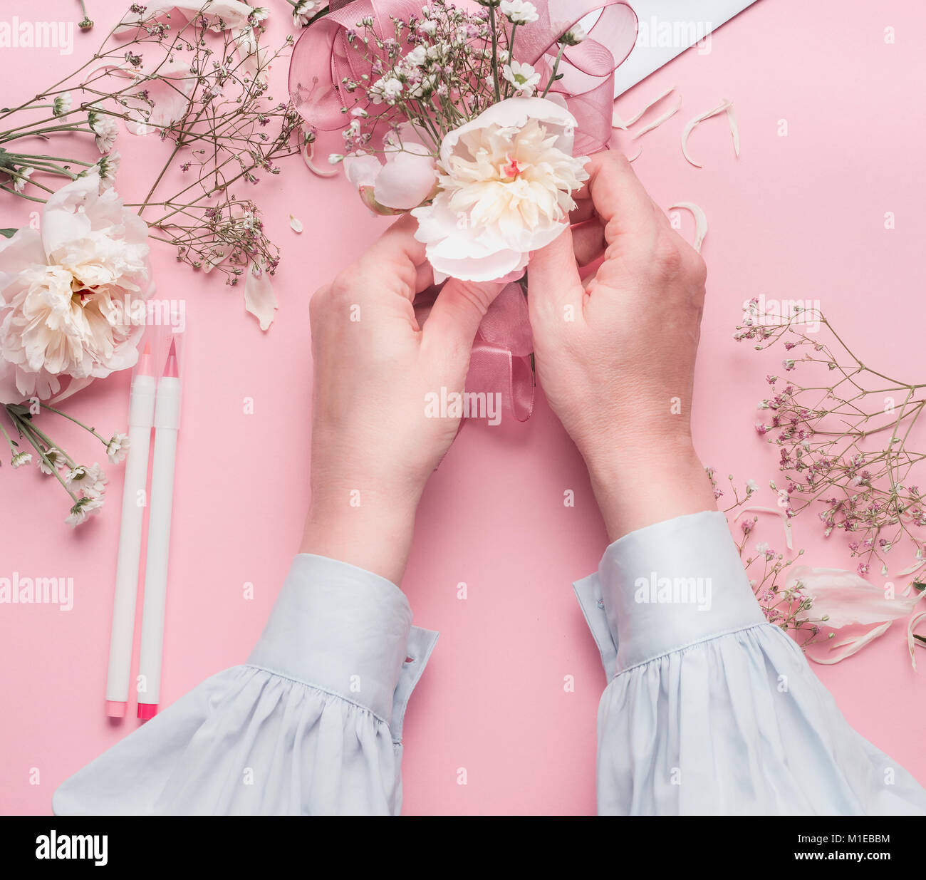 Mani femminili rendendo composizioni floreali con fiori di colore bianco al rosa pastello sfondo, vista dall'alto Foto Stock