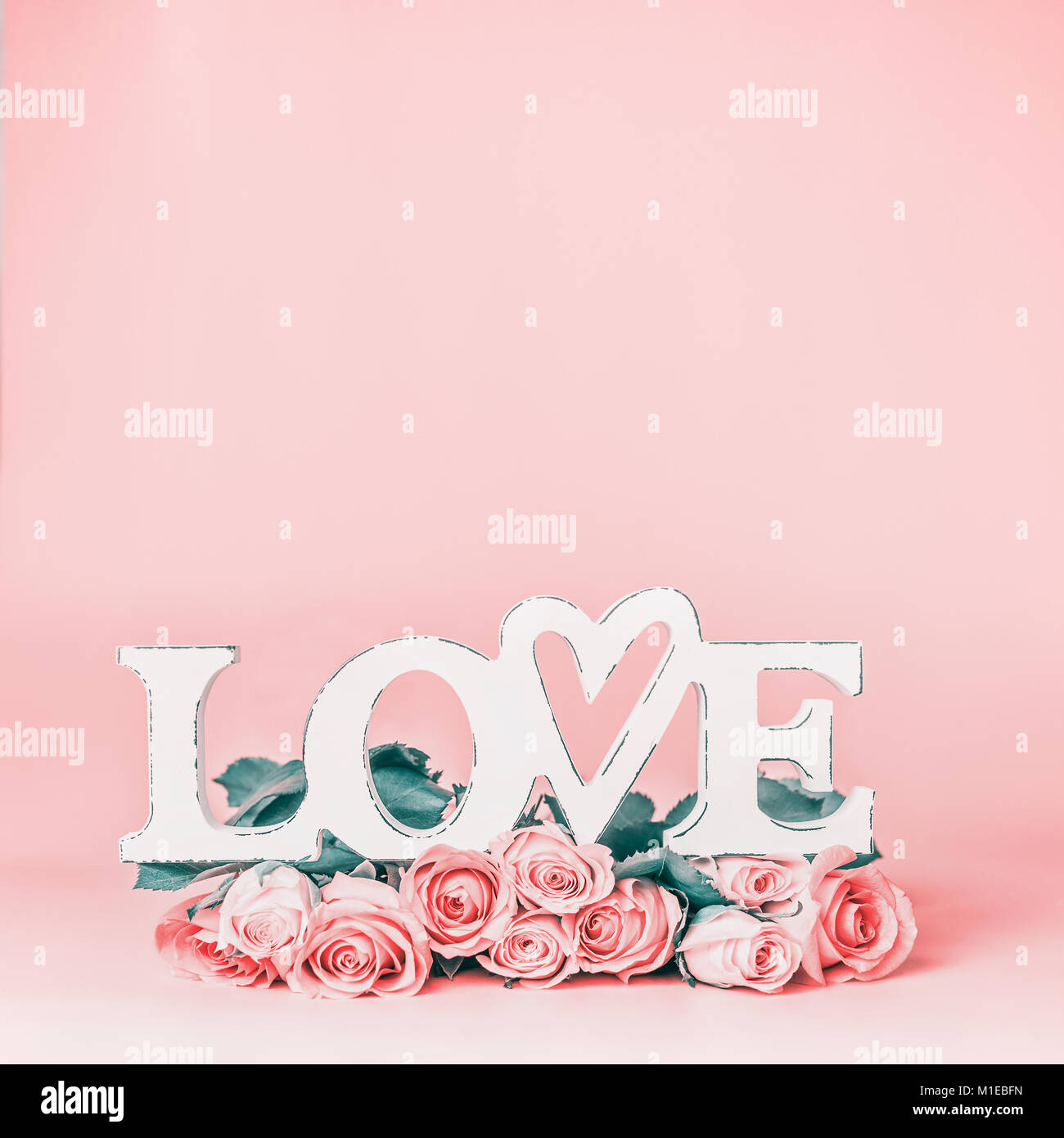 La parola amore pastello su sfondo rosa con un bellissimo mazzo di rose, vista frontale. Creative vacanze femmina formato con spazio di copia per il messaggio di saluto Foto Stock