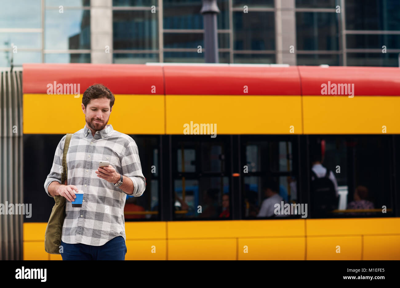 Giovane uomo in piedi alla fermata del bus tramite il suo cellulare Foto Stock