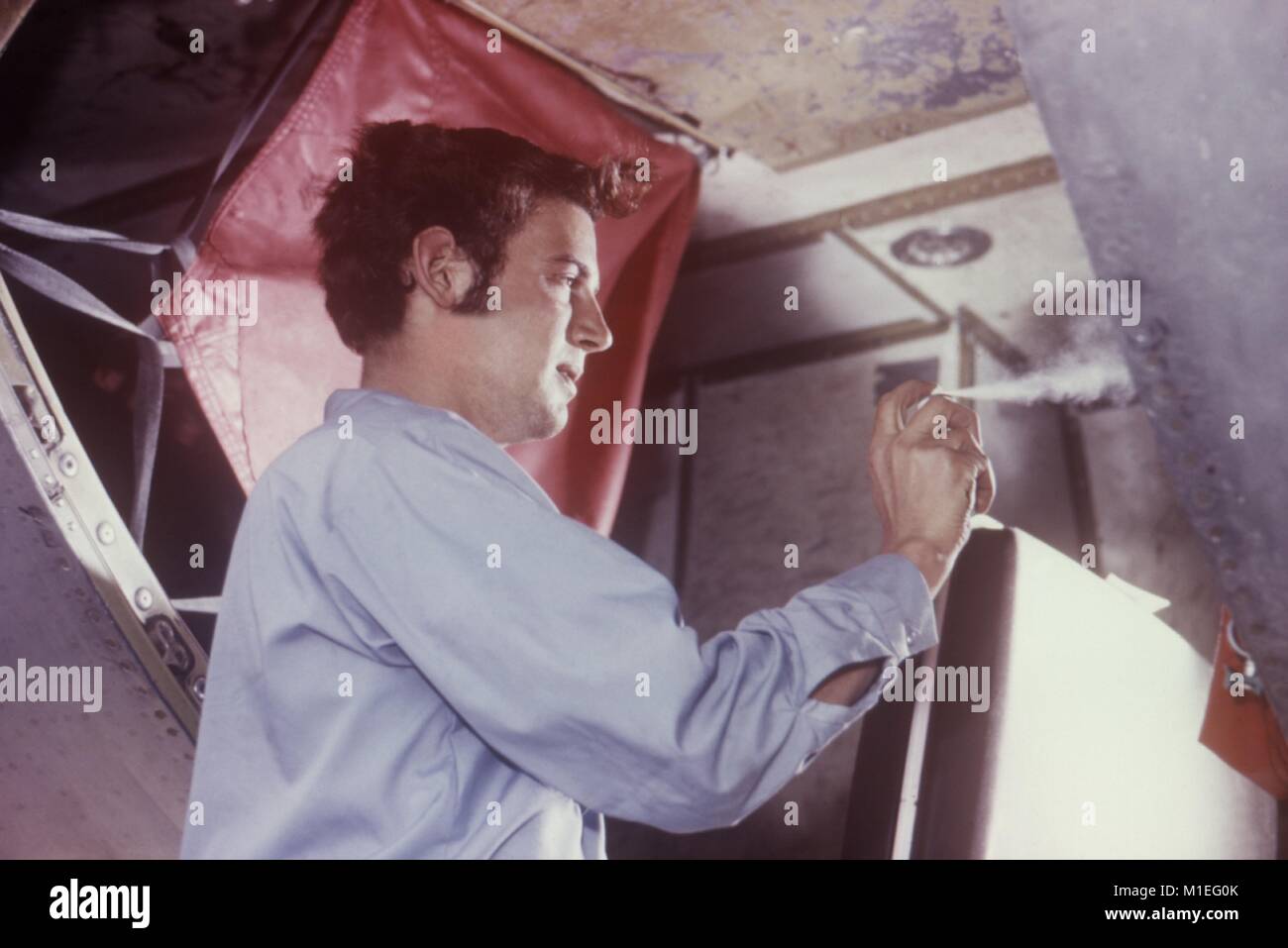 Dipendente della compagnia aerea di spruzzatura del vano di carico di un aeromobile con un aerosol insetticida spray, 1971. Immagine cortesia di centri per il controllo delle malattie (CDC). () Foto Stock