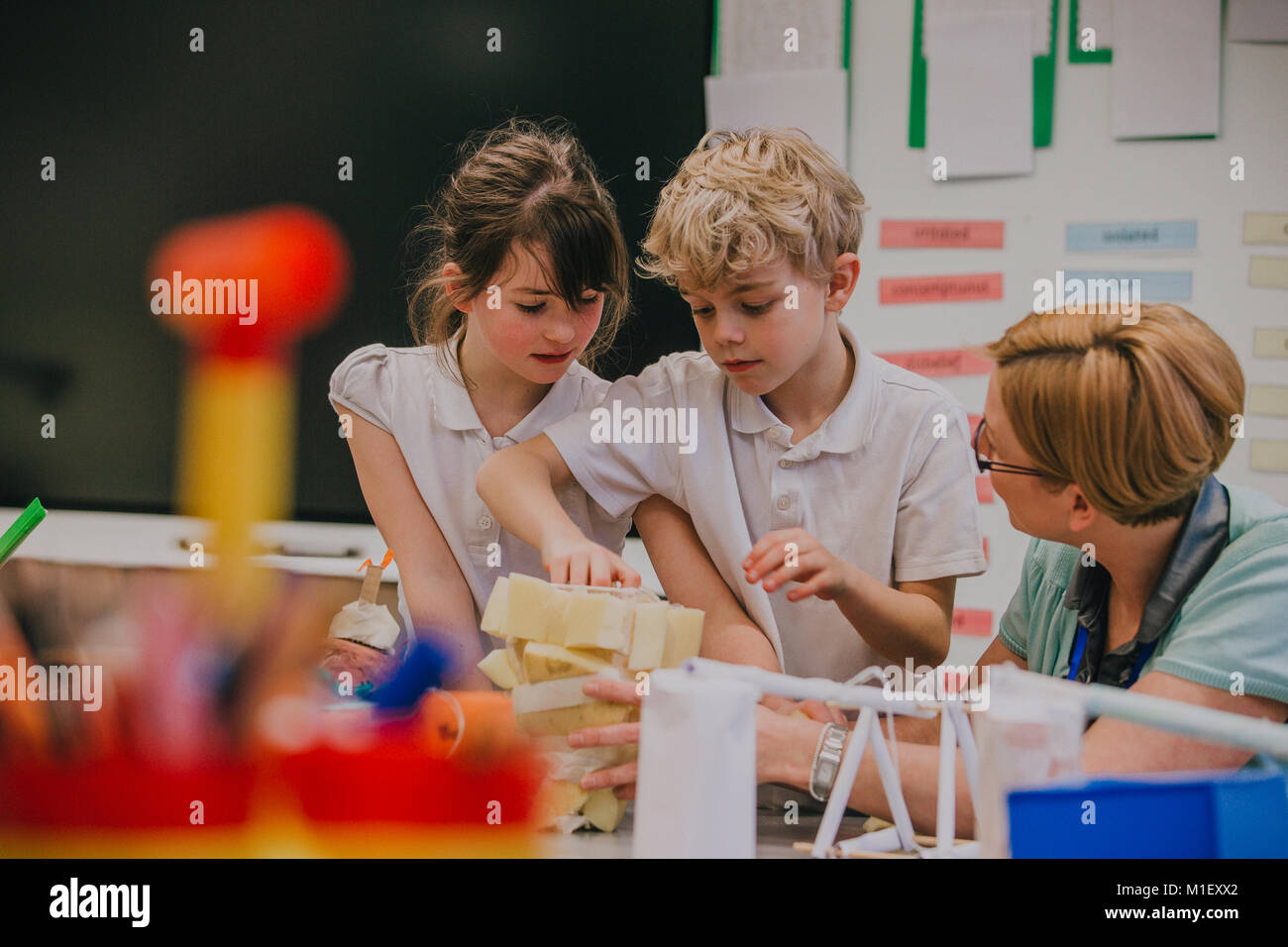 Studenti della scuola primaria sono al lavoro su un arti e mestieri progetto con il loro maestro. Essi sono la nastratura spugne insieme in una forma. Foto Stock