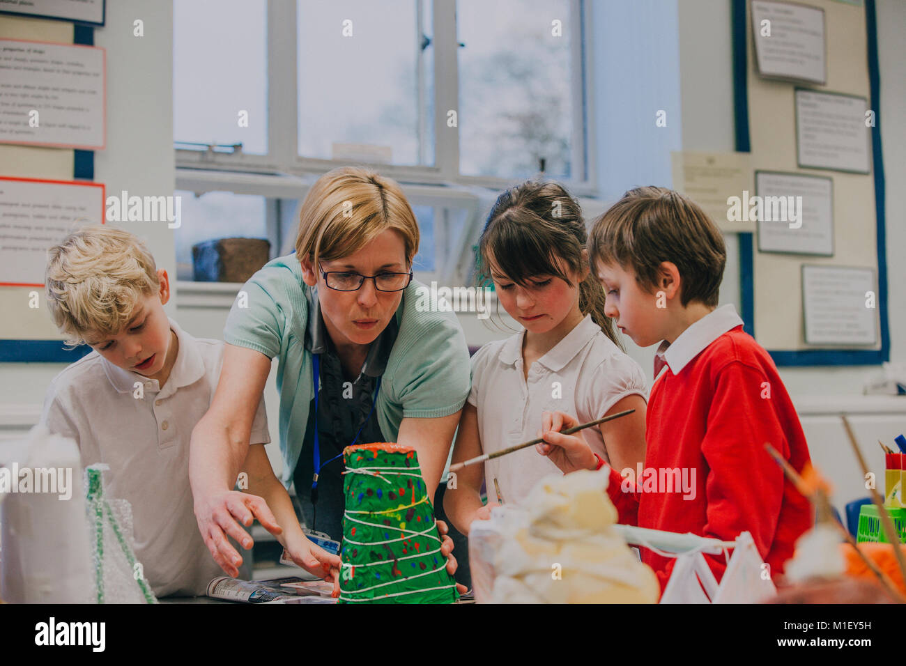 Studenti della scuola primaria stanno lavorando con il loro insegnante su un progetto di scienze in aula. Essi sono la realizzazione di una carta mache vulcano. Foto Stock