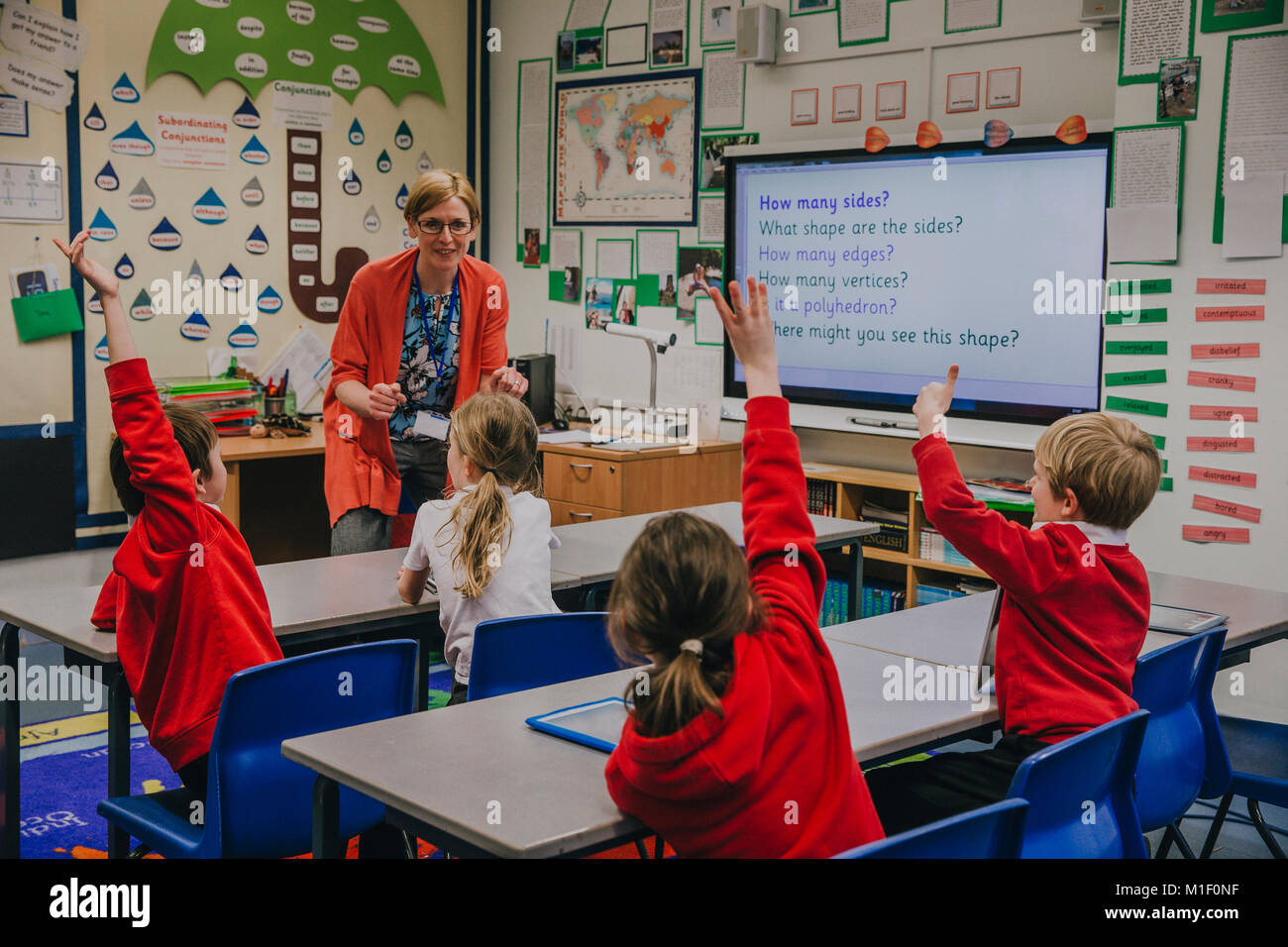 Femmina è insegnante di forme di insegnamento ai suoi studenti della scuola primaria. Ella chiede hem una domanda e alcuni degli studenti hanno la loro mano in aria per Foto Stock