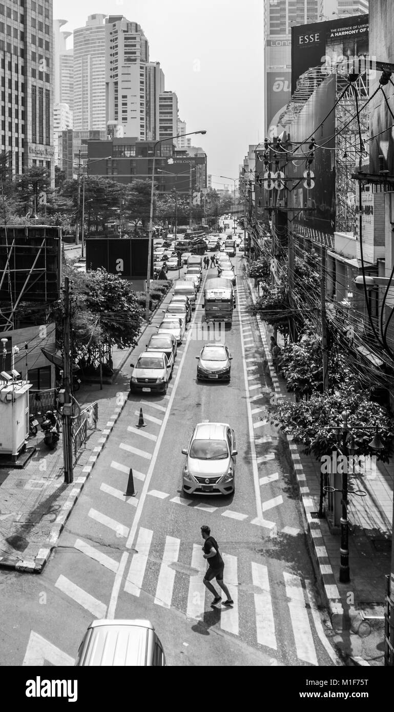 Dicembre 2017: una immagine in bianco e nero di un uomo che corre attraverso una trafficata strada di Bangkok. Foto Stock