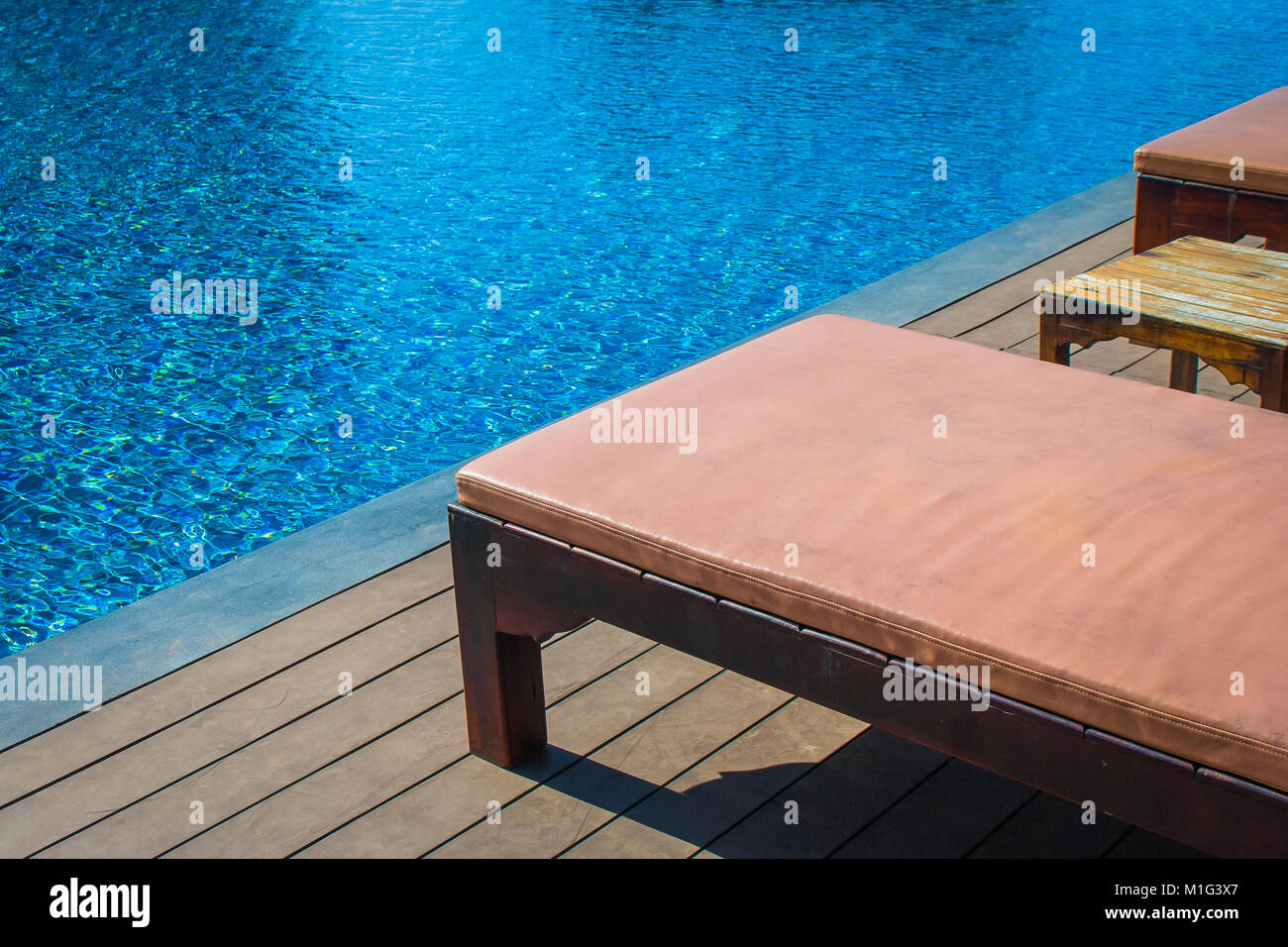 Concetto di rilassamento : dormeuse in legno impostazione sul pavimento di legno accanto alla piscina del resort. Foto Stock