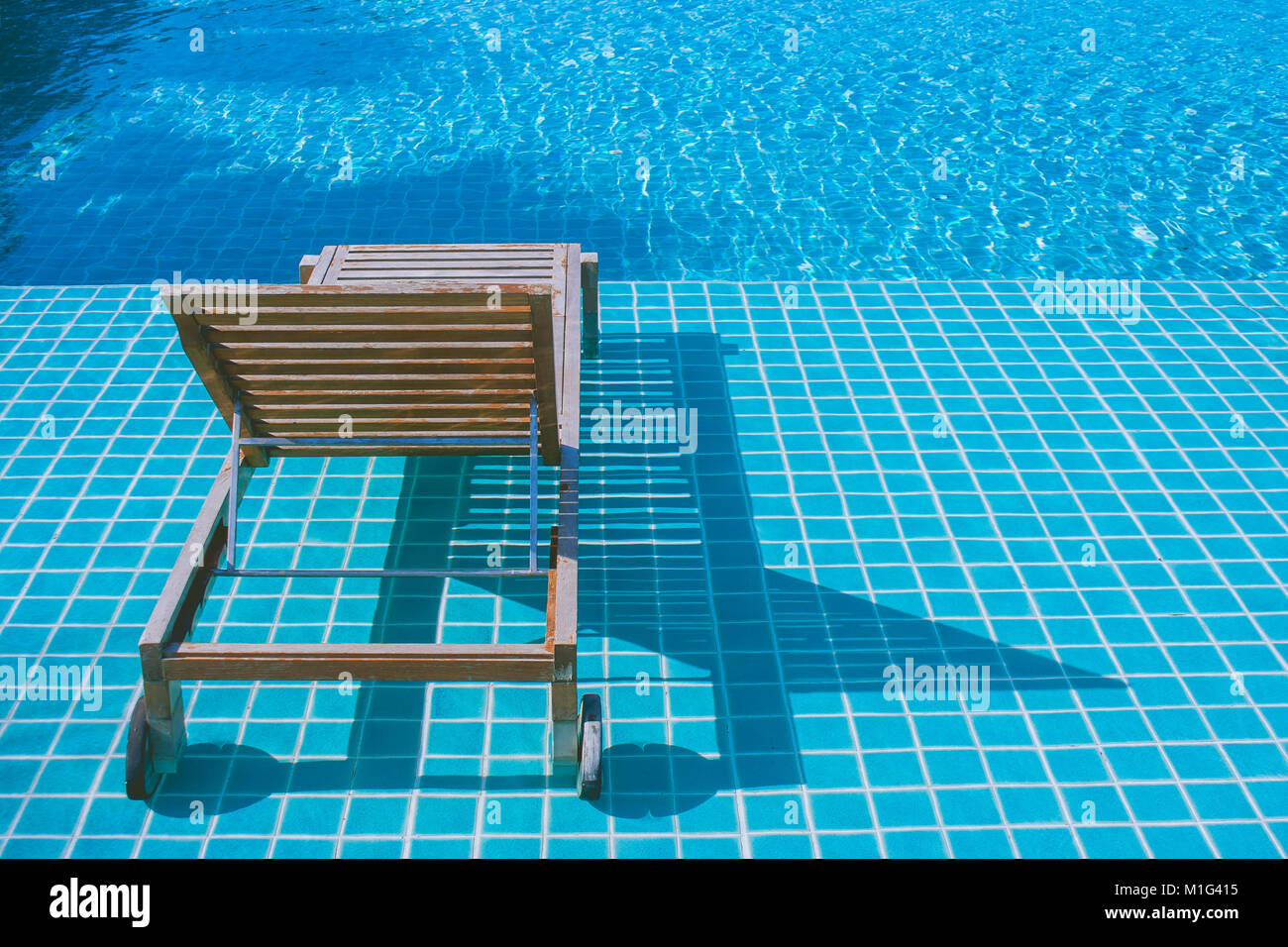 Concetto di rilassamento : dormeuse in legno impostazione su tessere di mosaico in piscina presso il resort. Foto Stock