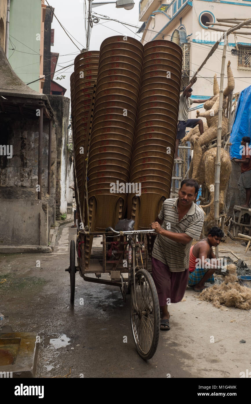Lavoratore in Kumartuli, vicino a Calcutta / Kolkata, West Bengal, India, spingendo un rickshaw sovraccaricato con un sacco di sedie attraverso il villaggio vicolo Foto Stock