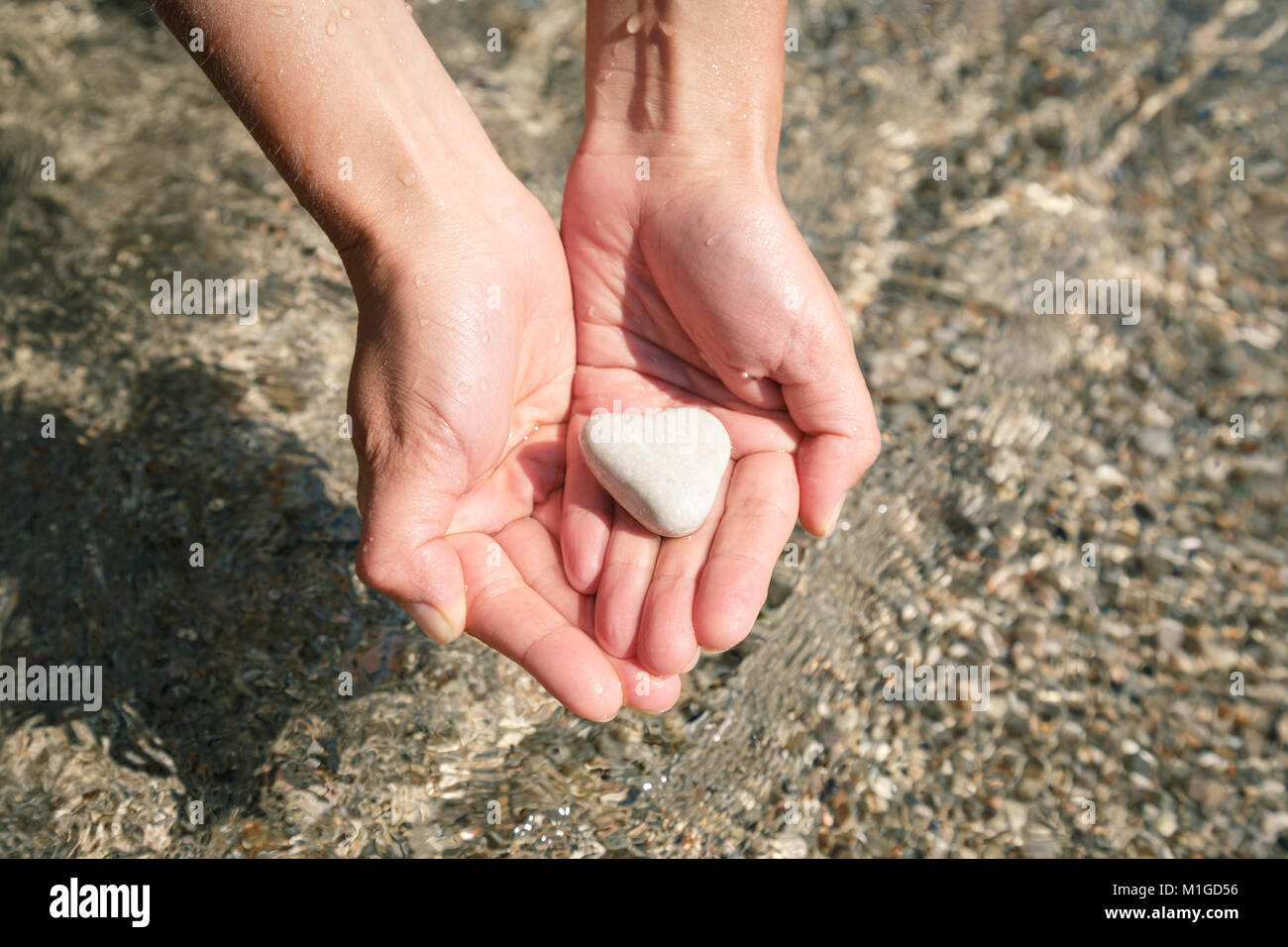 Vero cuore naturale a forma di pietra del mare nella donna lavato le mani dall'acqua di mare Foto Stock