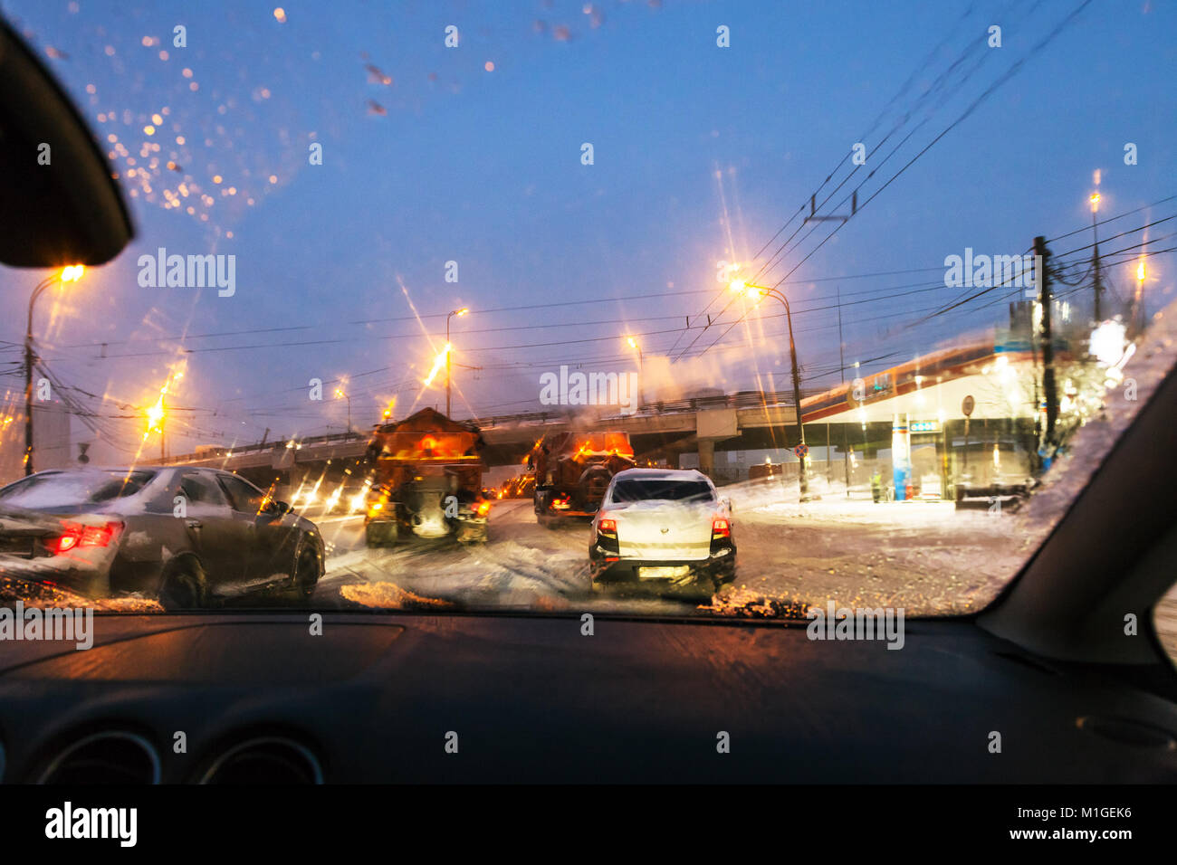 Vista di auto e strada di macchine di pulizia attraverso il parabrezza bagnato mentre si guida auto su strada nella città di Mosca in inverno sera nella neve Foto Stock