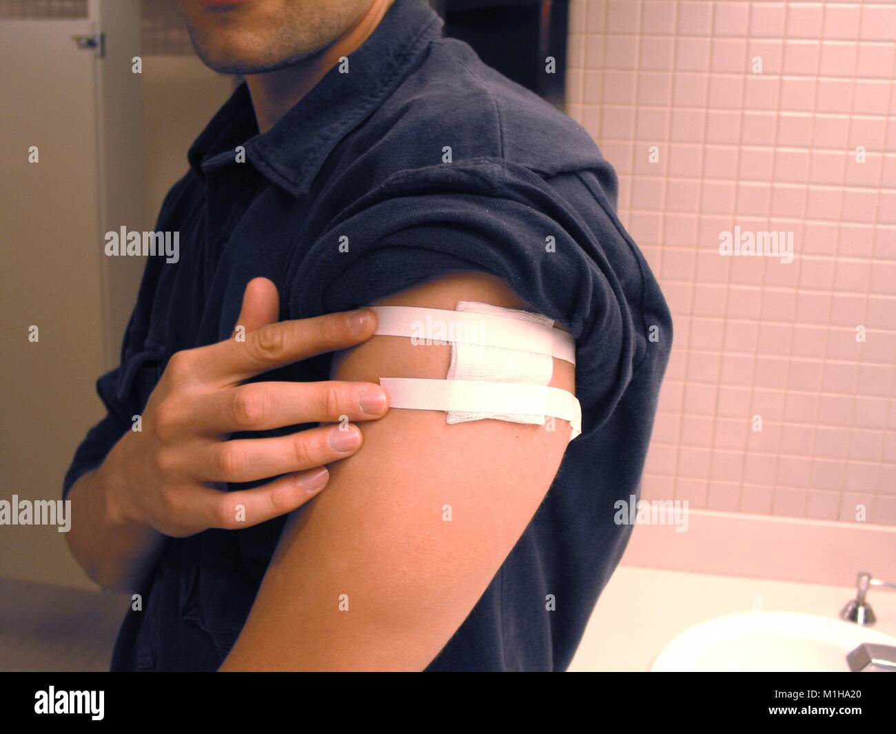 Un uomo di copertura di vaccinazione antivaiolo sito con la Benda di garza, close-up, all'restroom, presso i centri per il controllo delle malattie (CDC), Atlanta, Georgia, 2003. () Foto Stock
