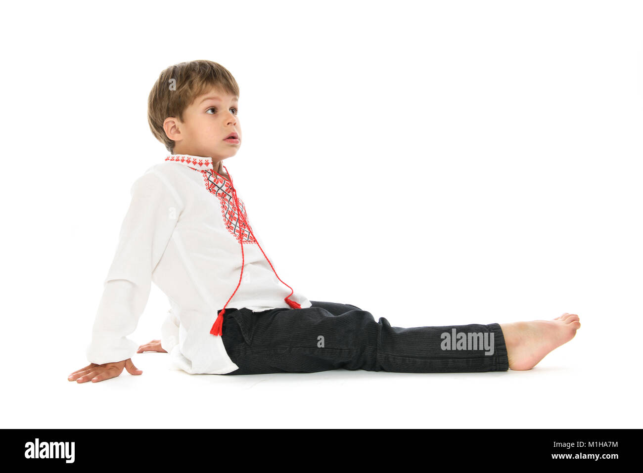 Little Boy in ucraino camicia ricamata a sedersi su sfondo bianco Foto Stock