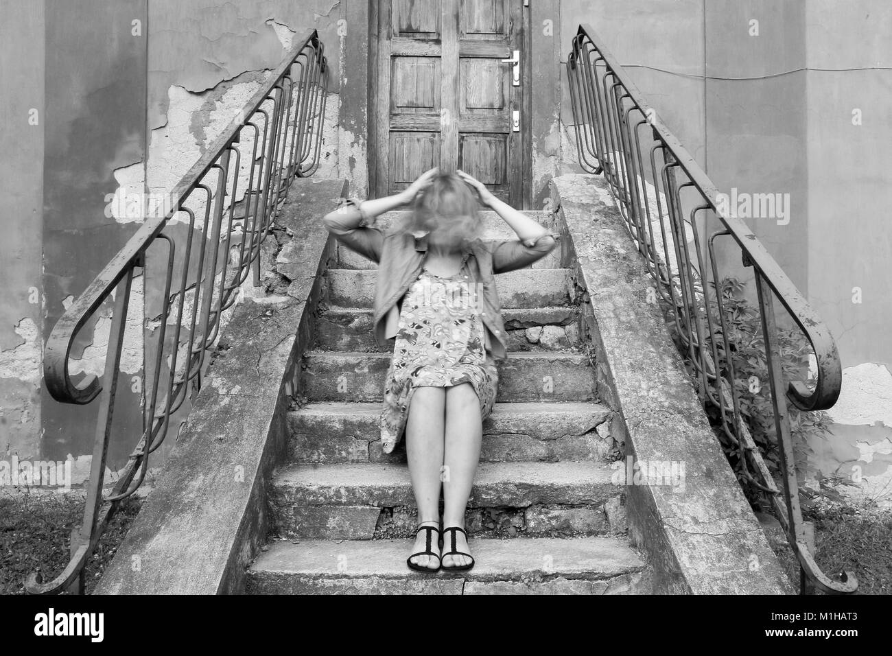 Una foto di una ragazza seduta sulle scale, tenendo la sua testa in movimento. Cerca confusi e smarriti. Foto Stock