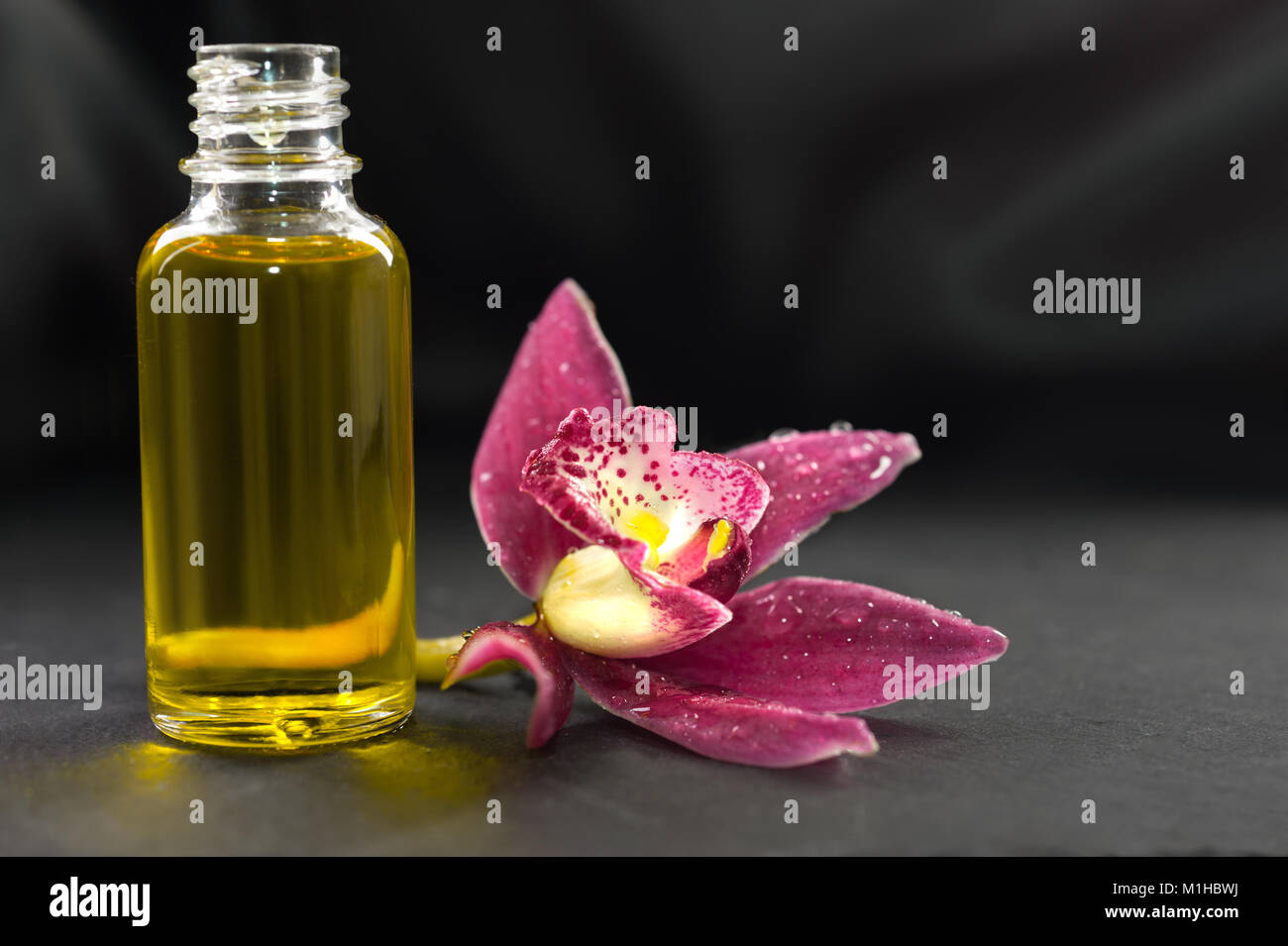 Welness background: olio aromatico di massaggio e di fiori di orchidea su sfondo scuro, spazio di testo Foto Stock