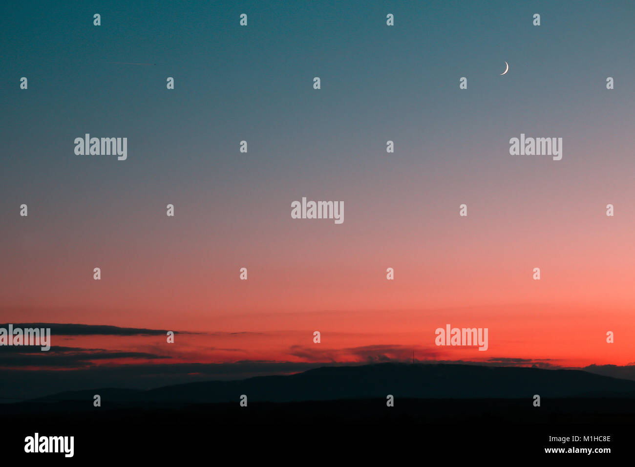 Una visione minimalista dal tramonto colorato. Le diverse sfumature di rosa e blu con la piccola Luna in alto nel cielo. Foto Stock