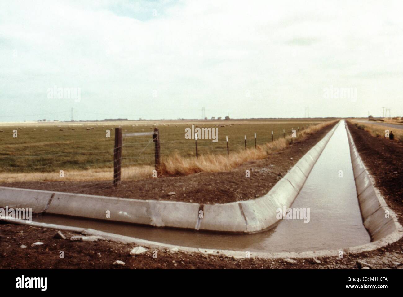 Fotografia di un calcestruzzo foderato di distribuzione di irrigazione canal passando accanto ad un pascolo recintato e una strada sull'altro lato, in California, un sito pertinenti per la CDC inchiesta del vettore di malattie in acqua risorsa sviluppi, 1976. Immagine cortesia CDC. () Foto Stock
