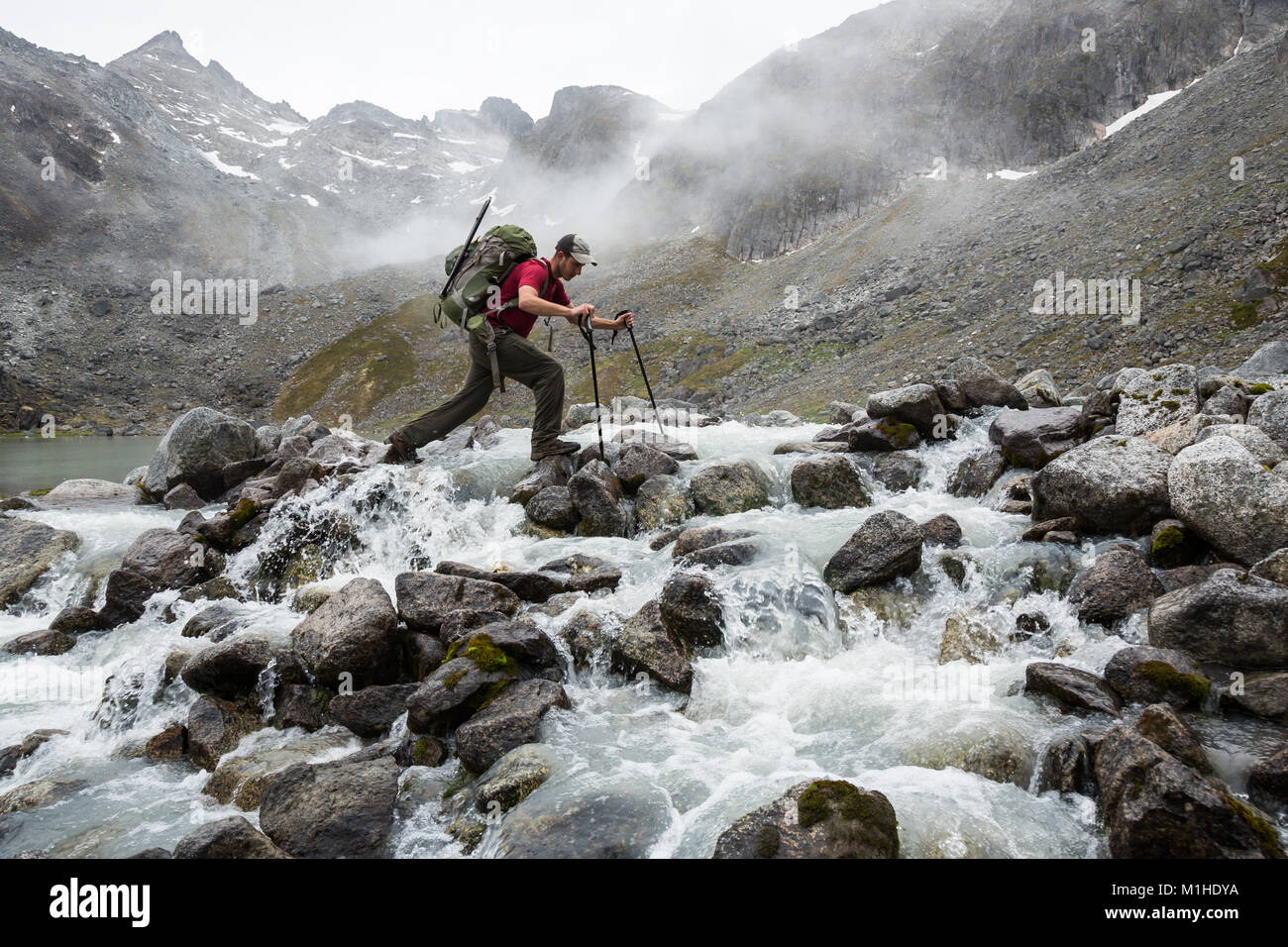 Un uomo passi il suo modo attraverso un rocky river nel deserto Talkeetna dell Alaska Foto Stock