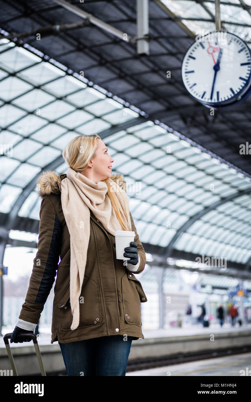 Donna che guarda l'orologio nella stazione ferroviaria di come il suo treno ha un ritardo Foto Stock