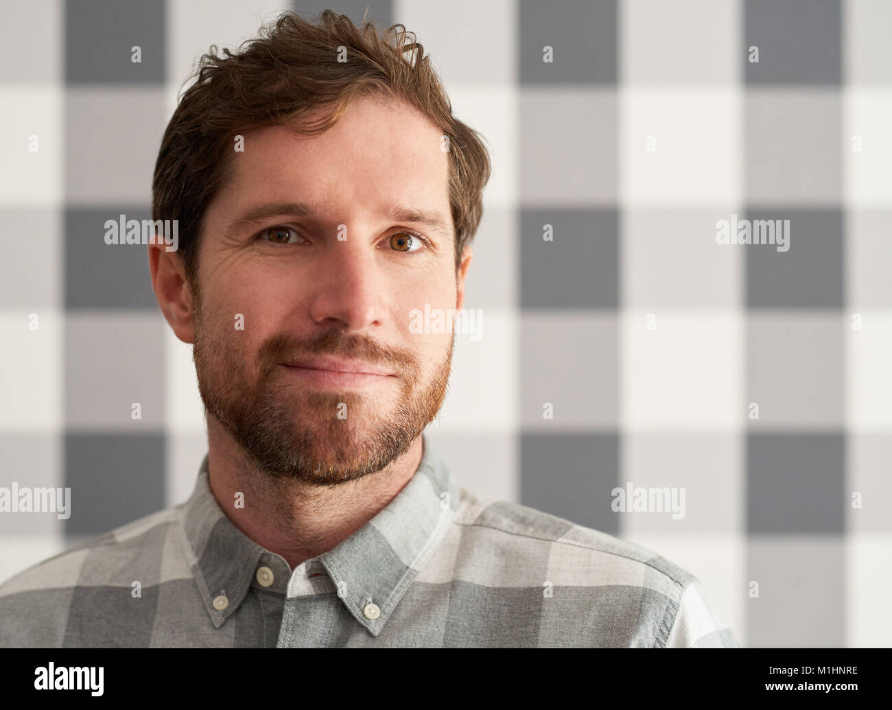 Contenuto giovane uomo che indossa una camicia matching il suo sfondo a scacchi Foto Stock