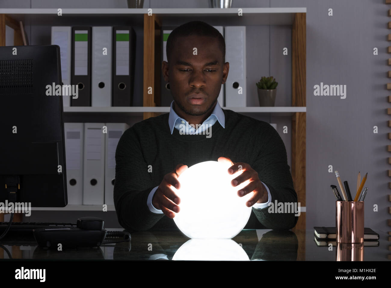 Ritratto di imprenditore africano predire il futuro con la sfera di cristallo sulla scrivania in ufficio Foto Stock