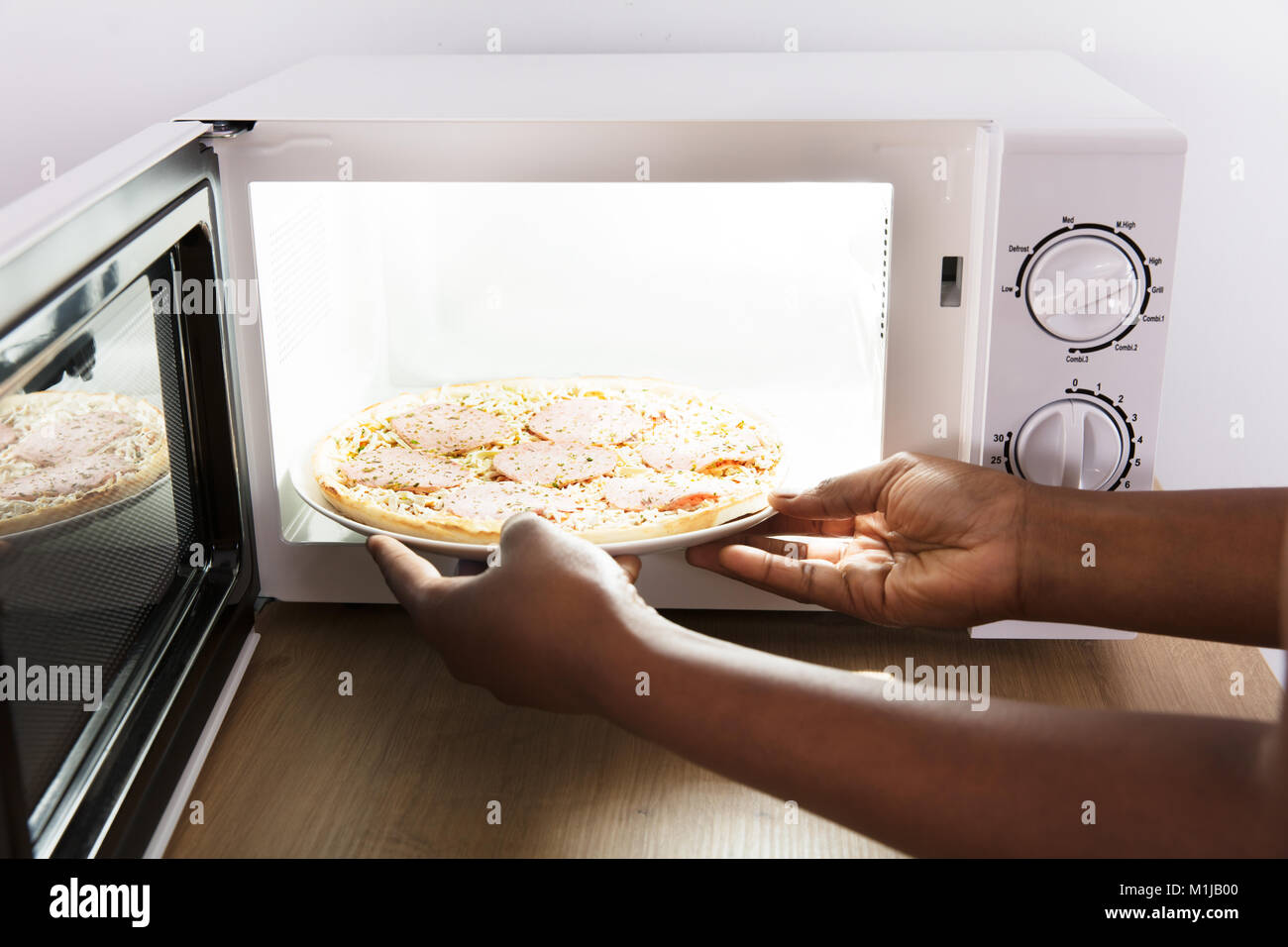 Close-up di una giovane donna africana cuocere la pizza in forno a microonde Foto Stock