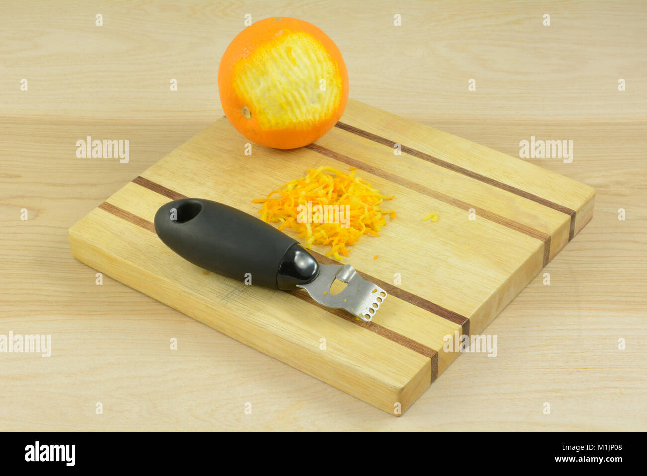 Arancione, scorza di arancia e zester arnese da cucina sul tagliere di legno Foto Stock