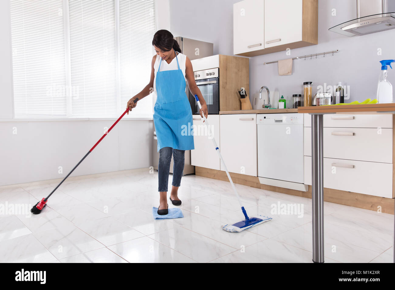 Casalinga Multitasking facendo i lavori di casa da spazzare e spandimento in cucina Foto Stock