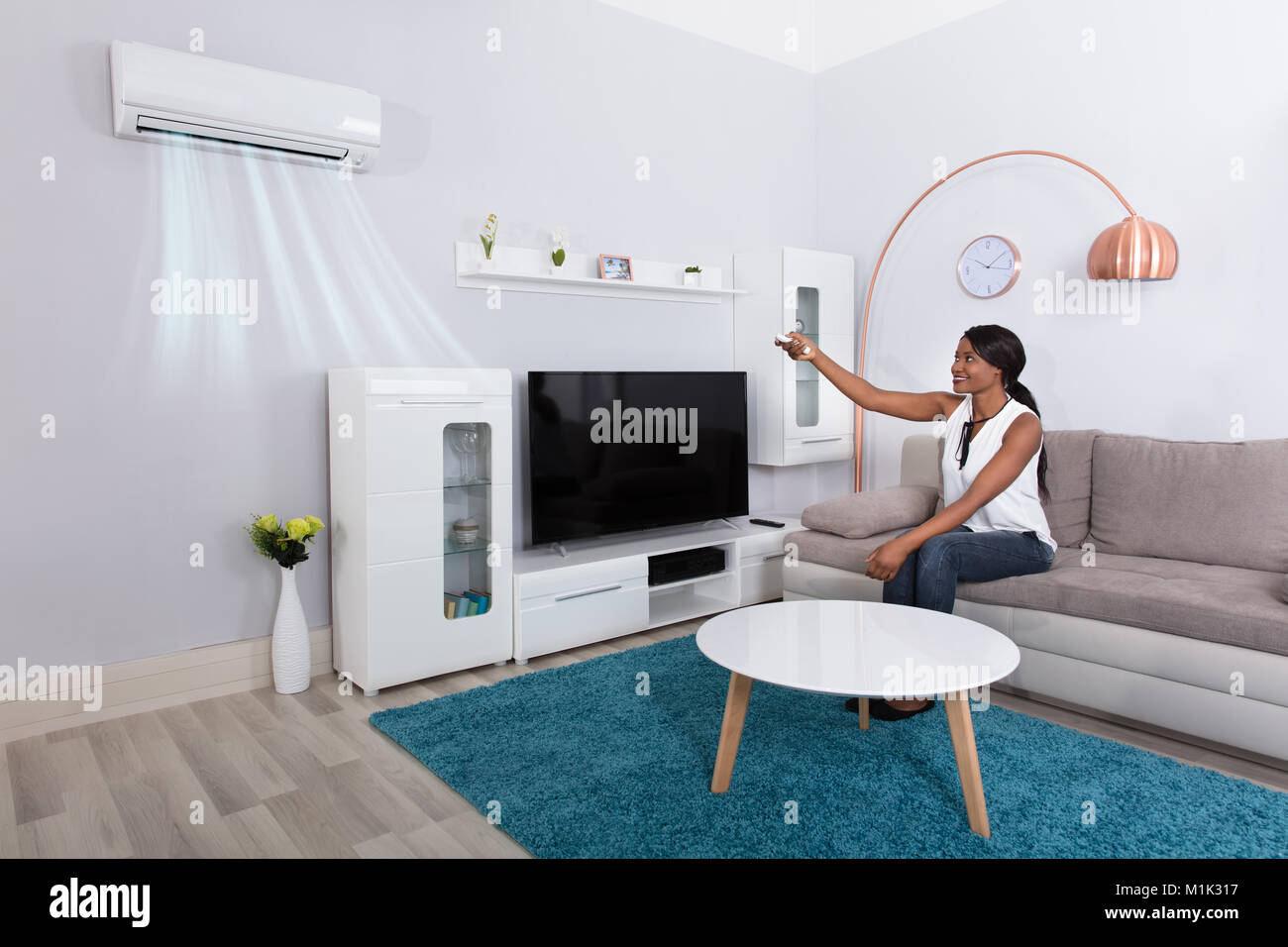 Felice donna africana seduto sul divano con il condizionatore d'aria di casa Foto Stock