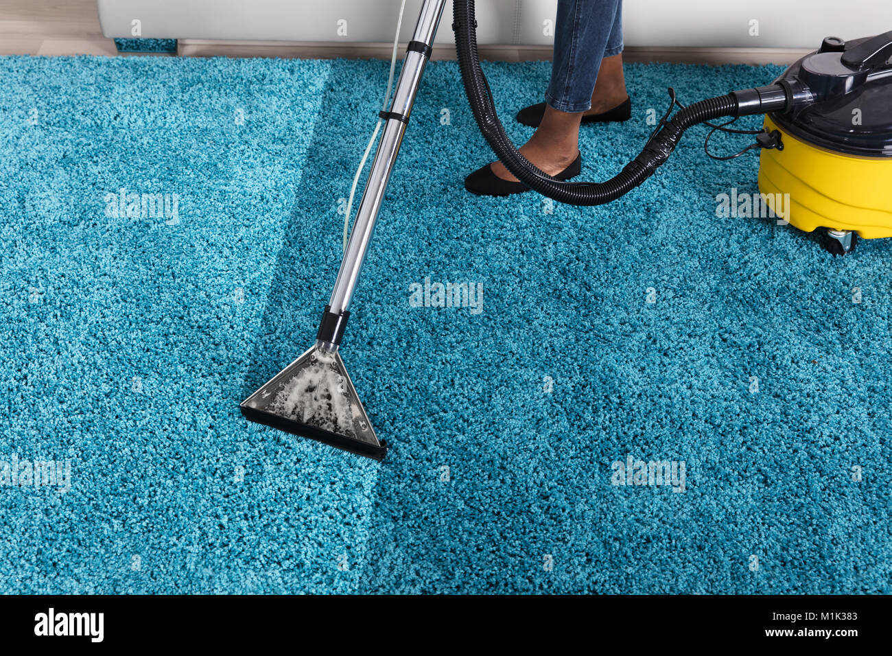Persona che utilizza un aspirapolvere per la pulizia di tappeti blu a casa  Foto stock - Alamy