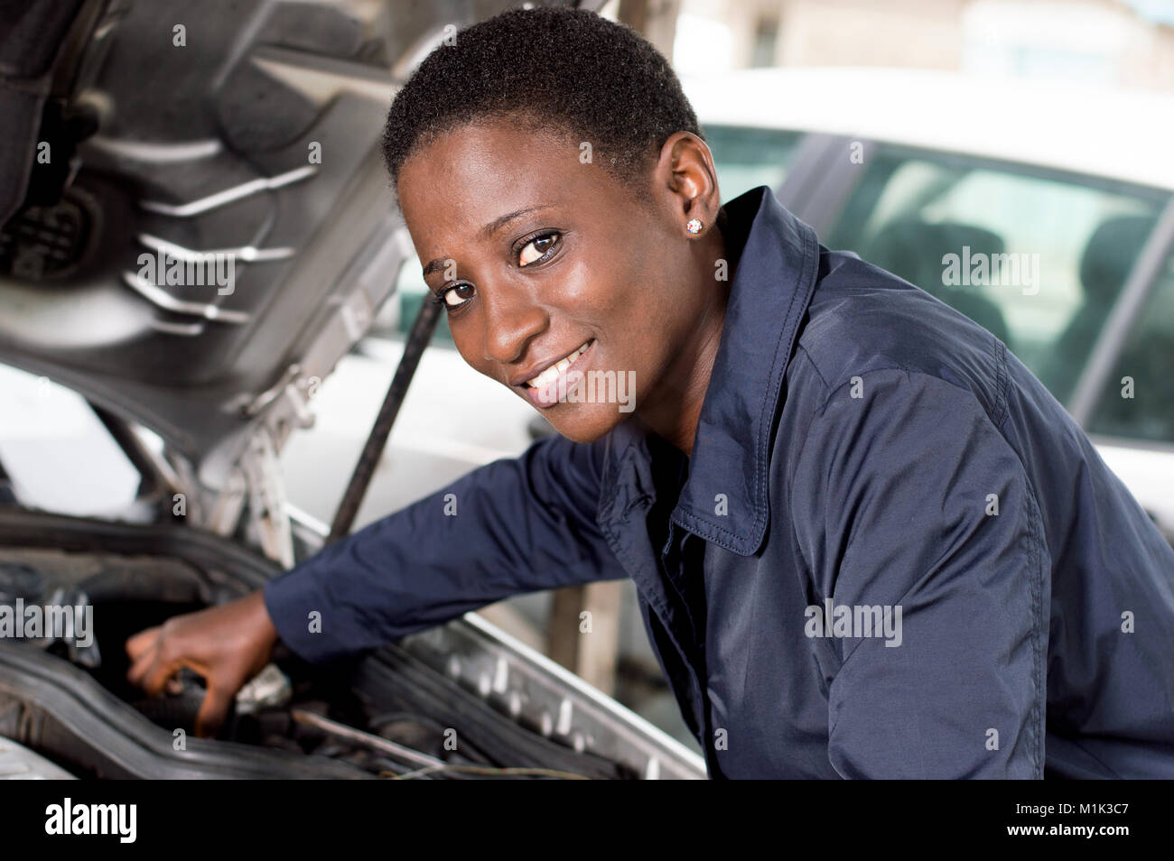Giovani femmine meccanico ripara una vettura mettendo il motore in buone condizioni. Foto Stock