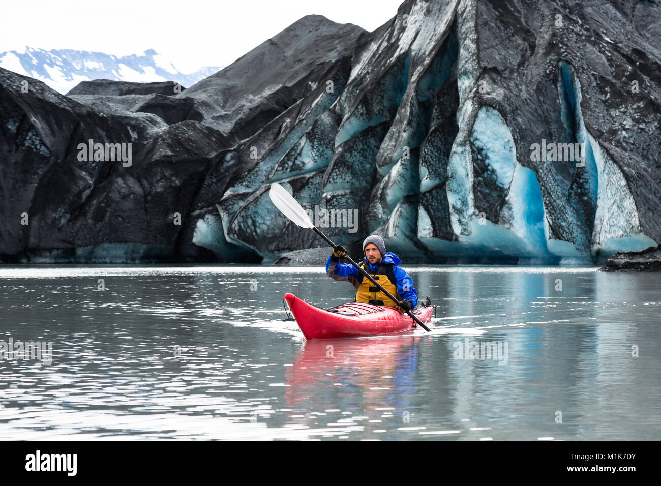 Un uomo pagaie suo kayak lontano dal terminale del ghiacciaio Spencer. Il ghiaccio è coperto con morena scuro - la sporcizia e la massa di roccia fino dal ghiacciaio. Foto Stock