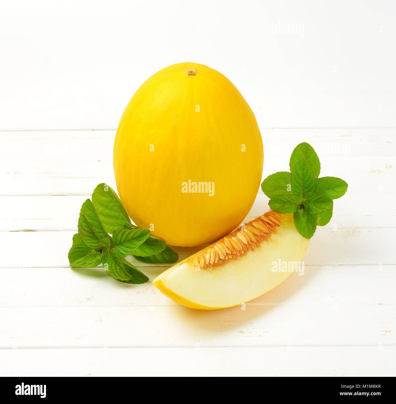 Freschi di melone giallo su bianco sullo sfondo di legno Foto Stock