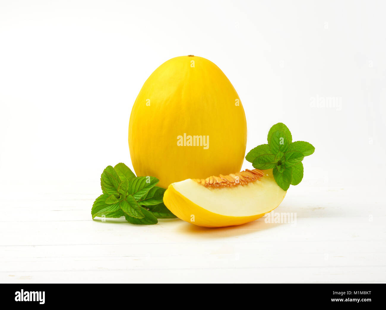 Freschi di melone giallo su bianco sullo sfondo di legno Foto Stock