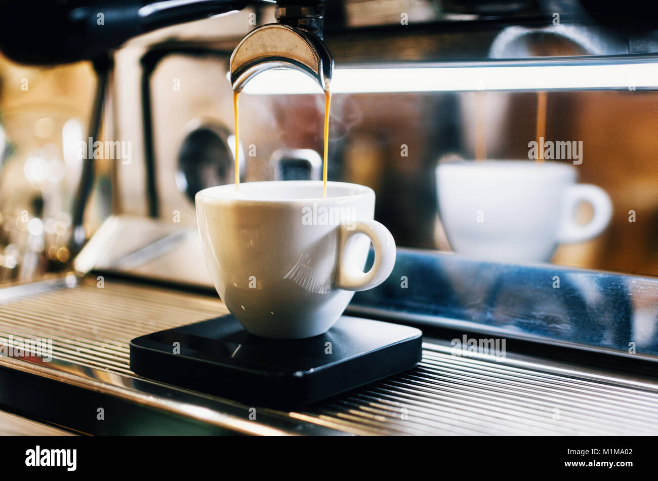 La macchina per espresso professionale versando il caffè fresco in bianco tazza ceramica con la riflessione sullo sfondo Foto Stock