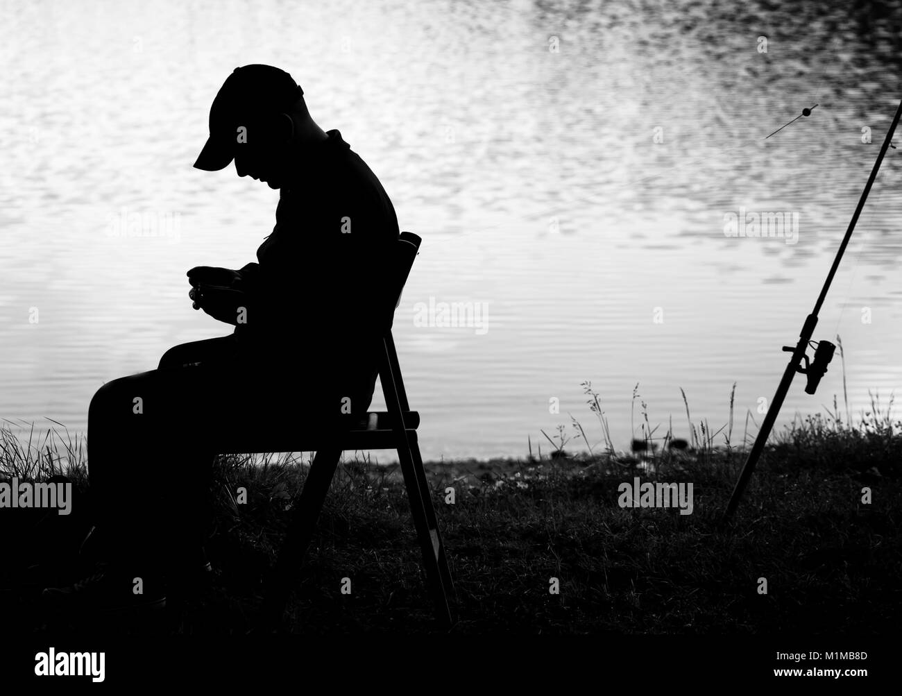 Bianco e nero silhouette pescatore vicino lago calmo Foto Stock