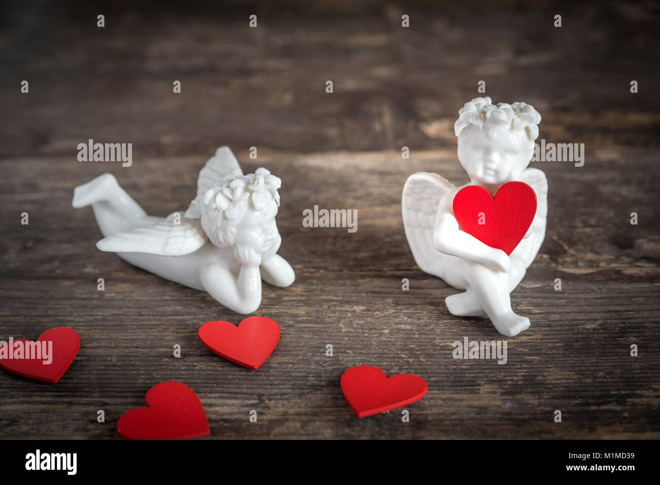 Due angeli di ceramica tenere cuori rossi. Essi sono qui seduti su un tavolo di legno Foto Stock