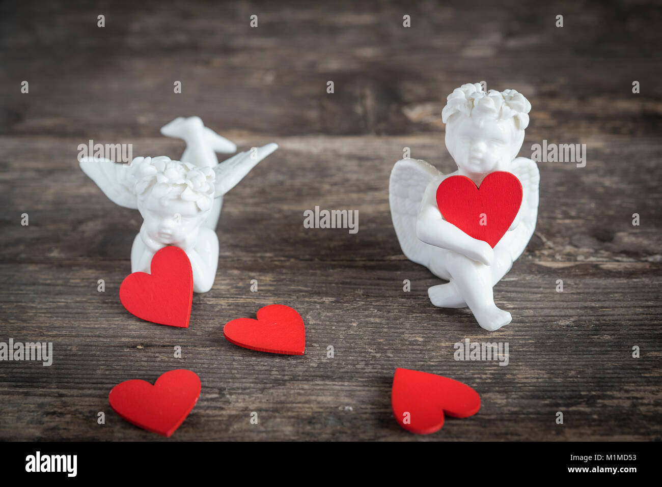 Due angeli di ceramica tenere cuori rossi. Essi sono qui seduti su un tavolo di legno Foto Stock