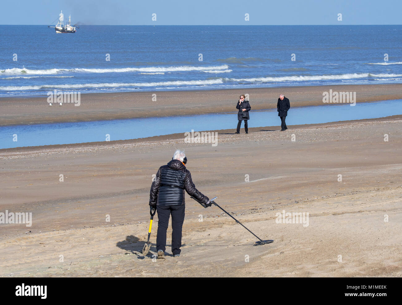 Donna anziana con il rivelatore di metalli beachcombing sulla spiaggia di sabbia lungo la costa del Mare del Nord in inverno Foto Stock