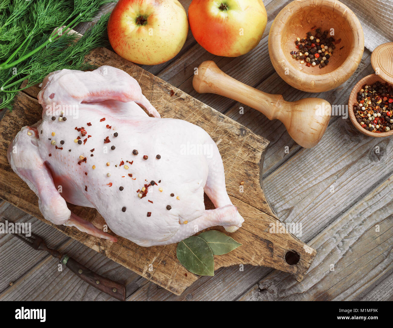 Carcassa di pollo su un sfondo di legno con spezie e mele, cucina in cucina, stile rustico Foto Stock