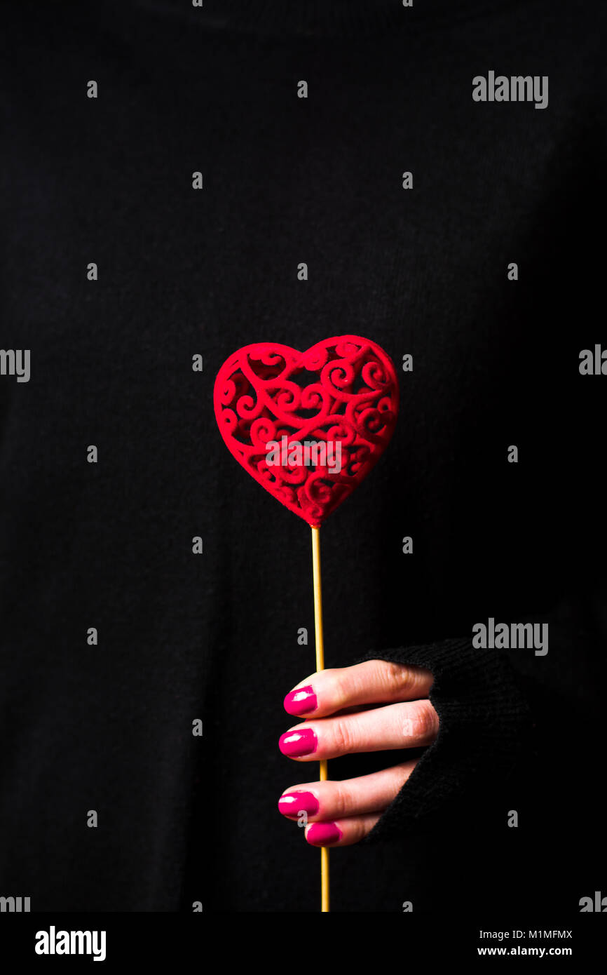 Azienda femmina a forma di cuore che indossa un maglione scuro su sfondo nero Foto Stock