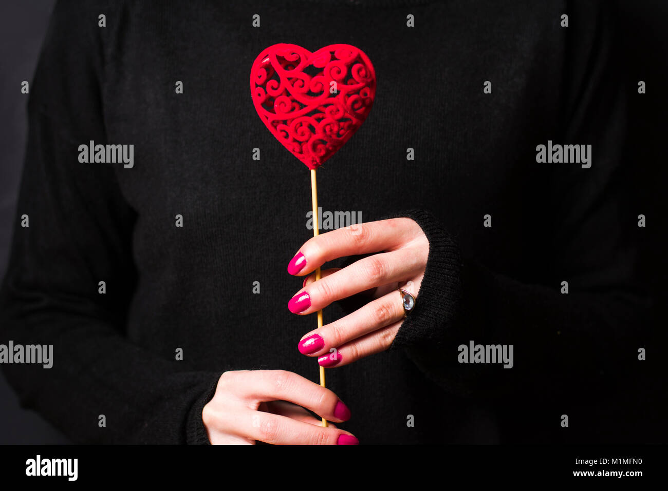 Azienda femmina a forma di cuore che indossa un maglione scuro su sfondo nero Foto Stock