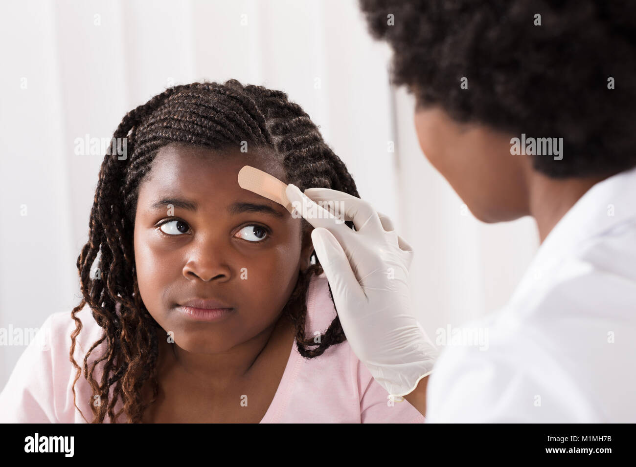 Close-up di un medico di applicare aiuti di banda alla testa di ragazza in clinica Foto Stock