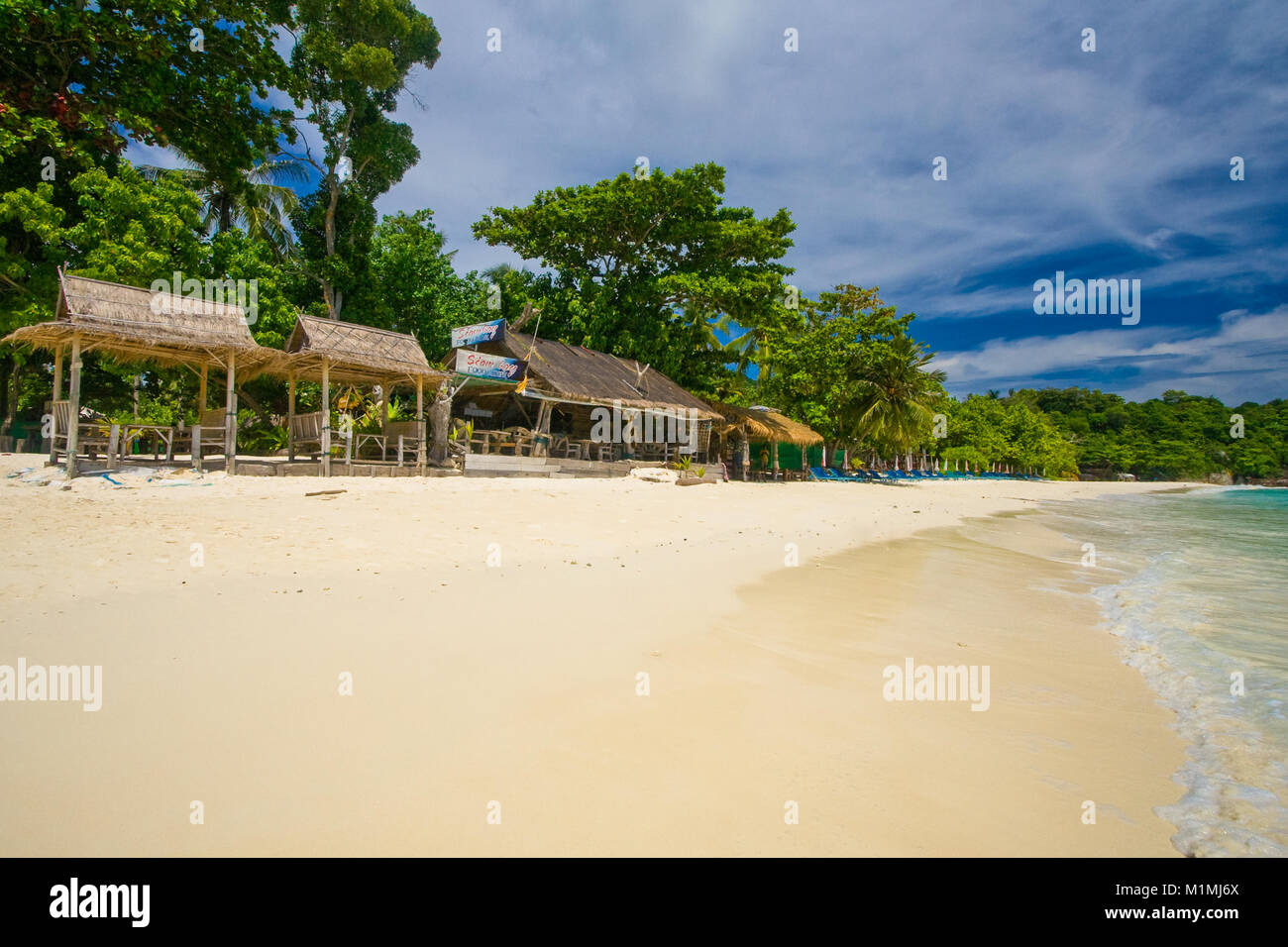 Una fila di strutture con foglie di palmo tetti di paglia sulla quasi vuoto bellissima spiaggia nella baia di Siam su Racha Island, Phuket, Tailandia. Foto Stock