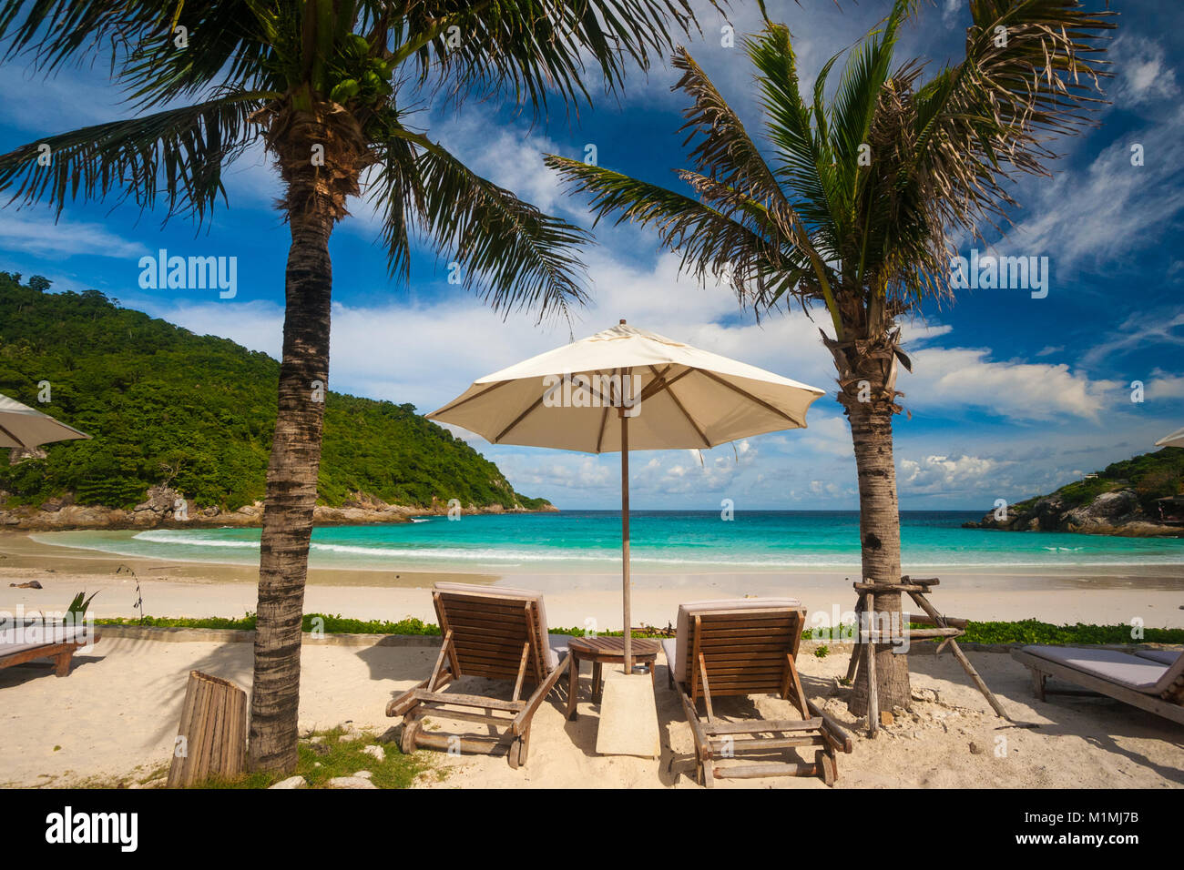 Una tipica vacanza bella scena con due sdraio e un ombrellone in tra, fiancheggiata da palme, offre una fantastica vista della spiaggia. Foto Stock