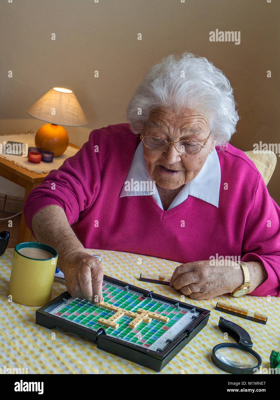 Anziani vulnerabili isolamento covid-19 CORONAVIRUS Lady Active brain word games anziani anziani anziani anziani 97 anni attivo allertamento vecchia signora di età godendo di una mente cervello-stimolante gioco di parola nel suo confortevole soggiorno, mentre godendo una tazza di tè in luce naturale finestra Foto Stock
