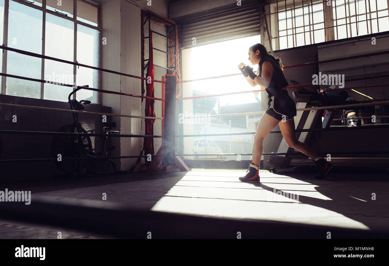 Boxer femmina facendo shadow boxing all'interno di un anello di inscatolamento. Boxer di praticare il pugilato si muove ad un boxing studio. Foto Stock