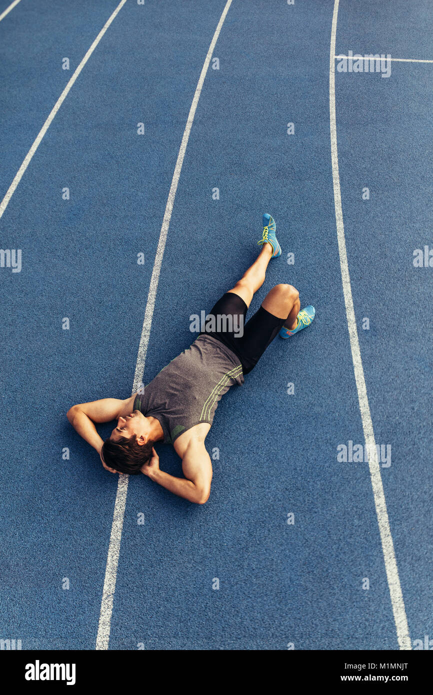 Runner giacente sulla via in un'atmosfera rilassata con le mani sotto la sua testa. Vista dall'alto di un atleta rilassante dopo una corsa. Foto Stock