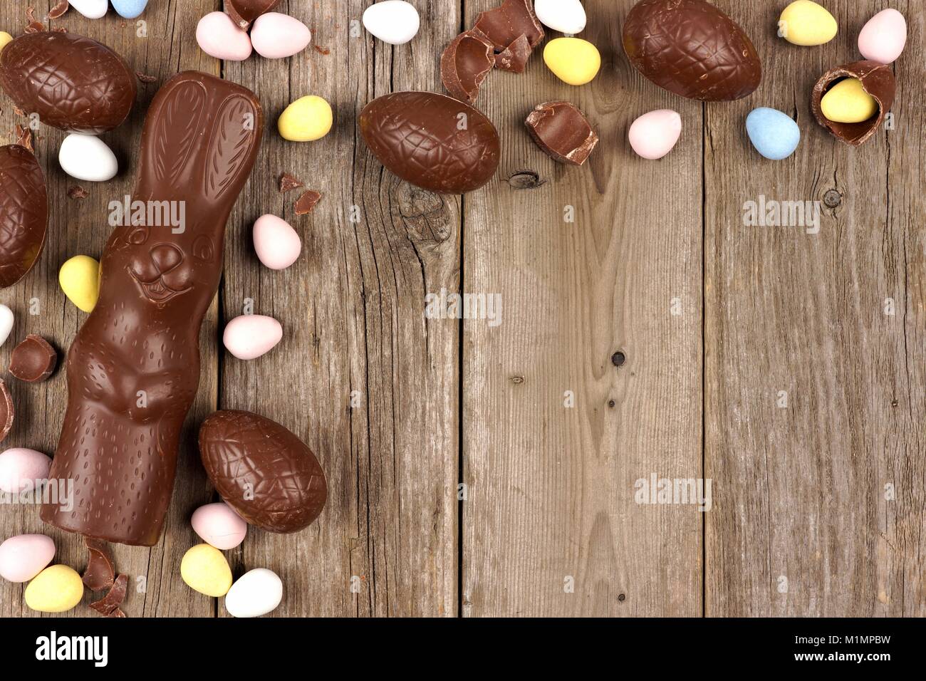 Uova di Pasqua di cioccolato con bunny formante un angolo bordo contro un rustico sfondo legno Foto Stock